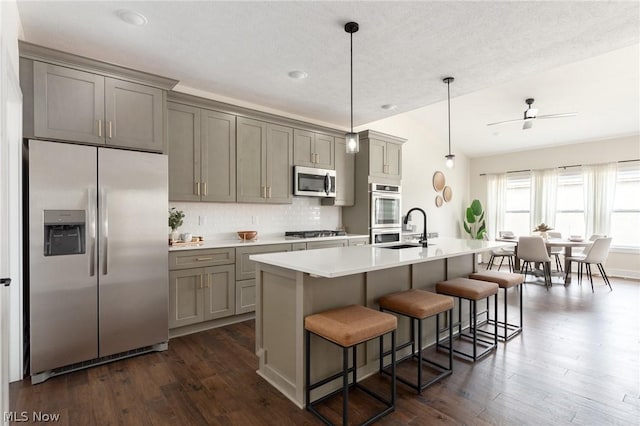 kitchen with a kitchen bar, sink, gray cabinetry, decorative light fixtures, and stainless steel appliances