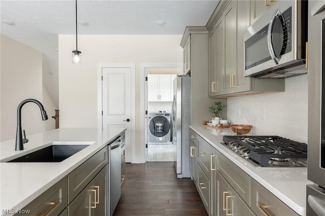 kitchen featuring pendant lighting, sink, gray cabinets, appliances with stainless steel finishes, and washer / dryer