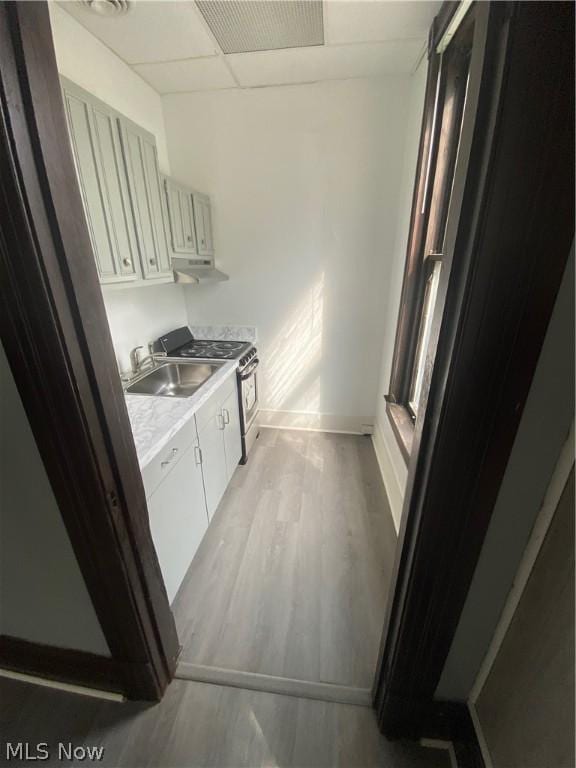 kitchen with sink, light hardwood / wood-style flooring, a paneled ceiling, white cabinetry, and stainless steel range with gas cooktop