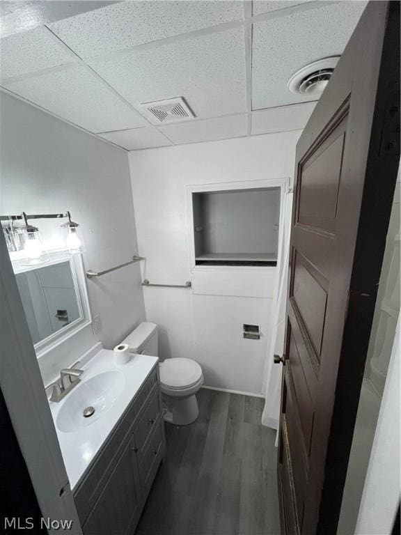 bathroom with wood-type flooring, toilet, vanity, and a drop ceiling