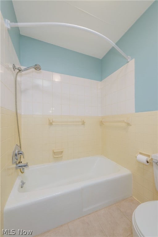 bathroom with tile patterned floors, tiled shower / bath, tile walls, and toilet