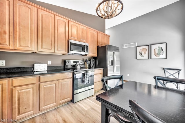 kitchen with lofted ceiling, an inviting chandelier, stainless steel appliances, light hardwood / wood-style floors, and hanging light fixtures