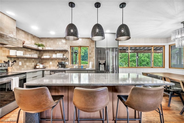 kitchen featuring pendant lighting, decorative backsplash, light stone counters, light hardwood / wood-style floors, and appliances with stainless steel finishes