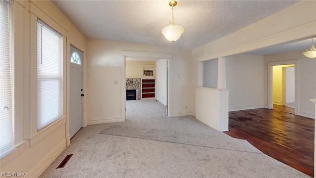 carpeted entryway featuring a stone fireplace and a textured ceiling