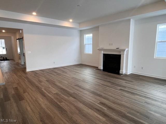 unfurnished living room featuring a wealth of natural light and dark wood-type flooring