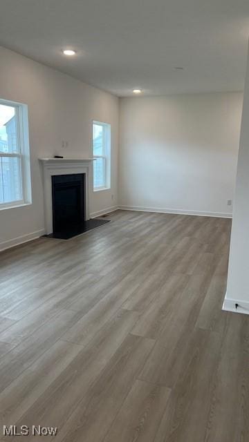 unfurnished living room with baseboards, recessed lighting, a fireplace, and light wood-style floors