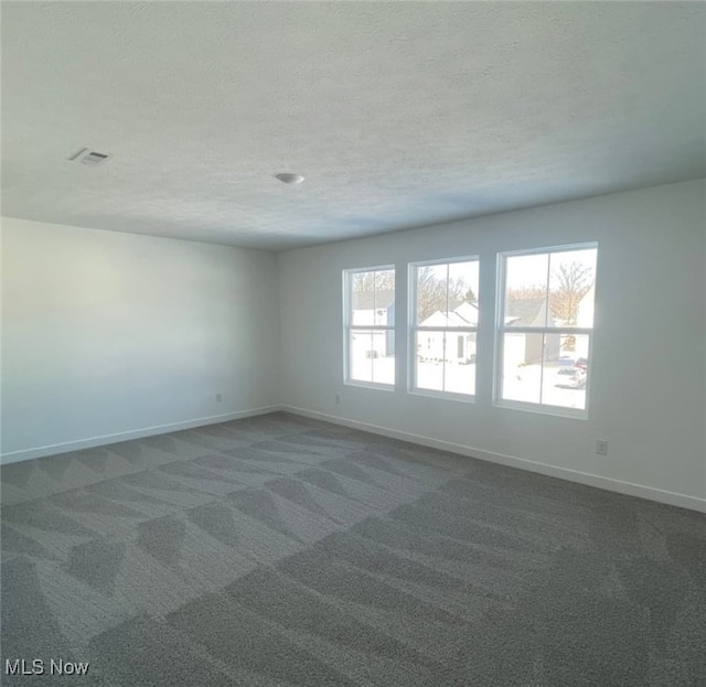 unfurnished room with a textured ceiling, dark carpet, visible vents, and baseboards