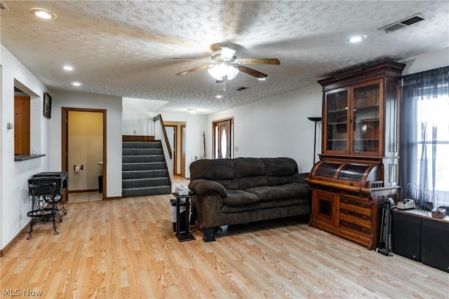 living room featuring ceiling fan, a textured ceiling, and light wood-type flooring