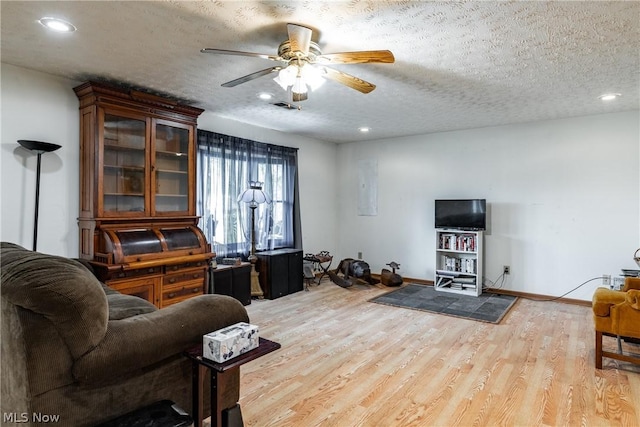 living room with ceiling fan, a textured ceiling, and light wood-type flooring