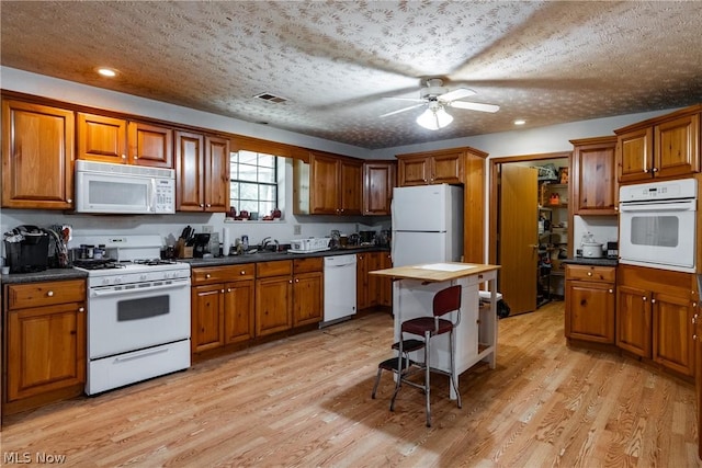 kitchen with white appliances, light hardwood / wood-style flooring, a breakfast bar area, ceiling fan, and a textured ceiling