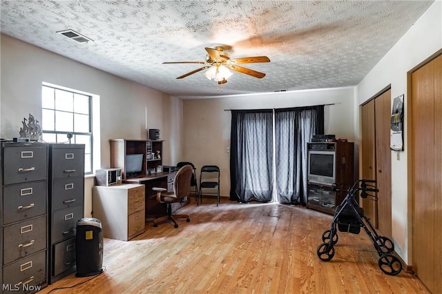 home office with ceiling fan, light hardwood / wood-style floors, and a textured ceiling