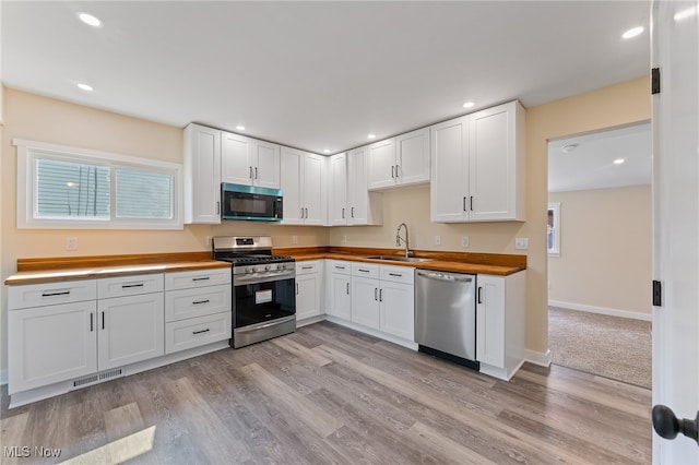 kitchen with appliances with stainless steel finishes, white cabinets, butcher block counters, light hardwood / wood-style flooring, and sink