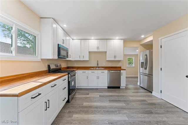 kitchen with appliances with stainless steel finishes, light hardwood / wood-style floors, white cabinetry, wood counters, and sink