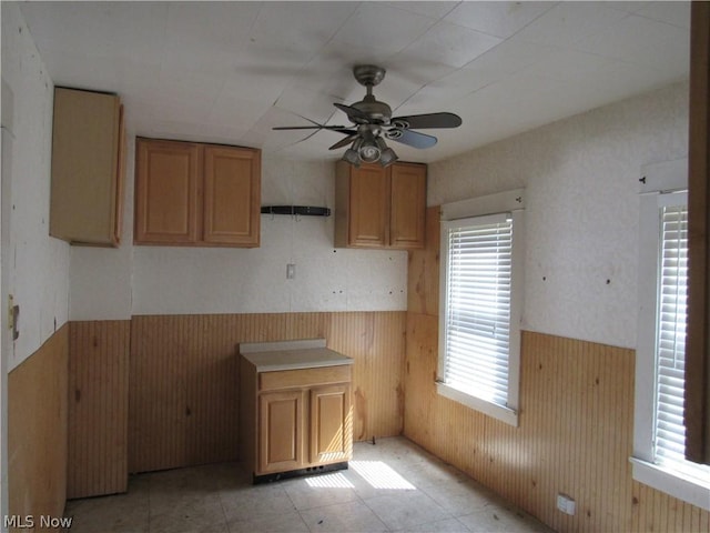 kitchen with ceiling fan, wooden walls, brown cabinetry, and wainscoting