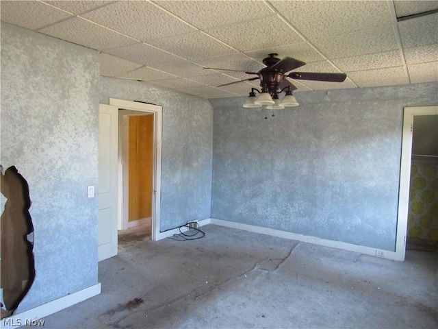 spare room featuring a drop ceiling, baseboards, concrete floors, and a ceiling fan