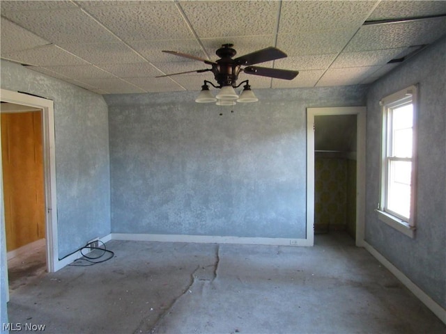 empty room with a ceiling fan, unfinished concrete floors, a paneled ceiling, and baseboards