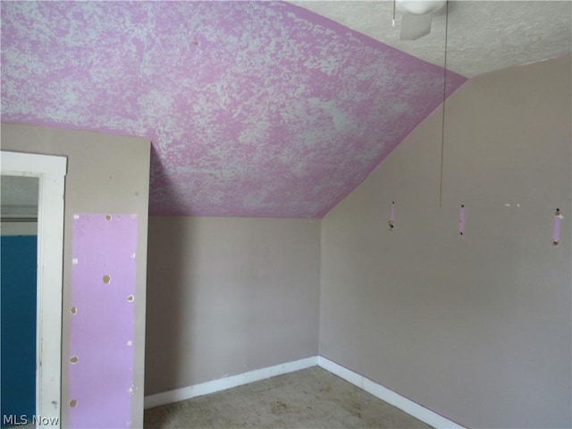 additional living space featuring vaulted ceiling, carpet, baseboards, and a textured ceiling