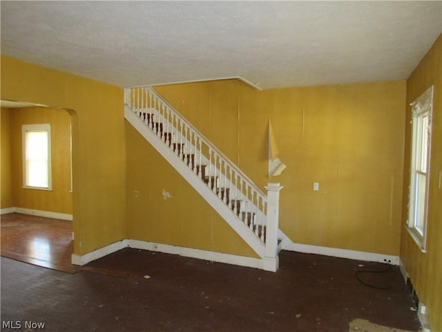 unfurnished living room featuring stairway, baseboards, and arched walkways