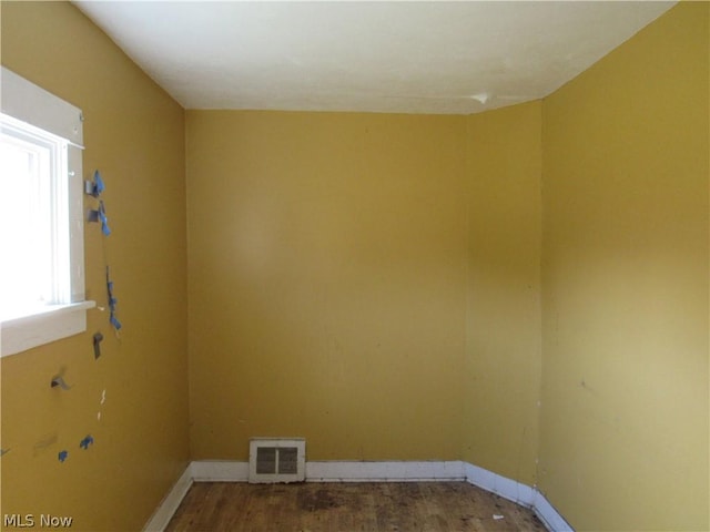 spare room with wood finished floors, visible vents, and baseboards