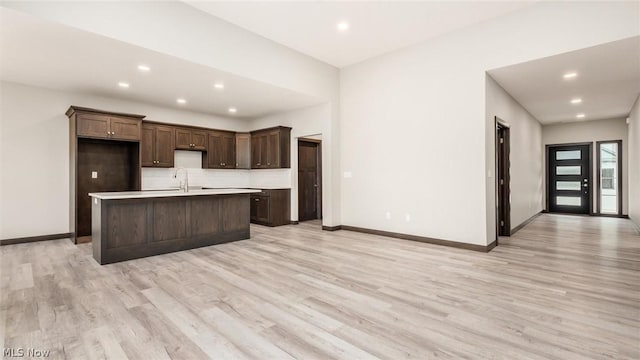 kitchen with a kitchen island with sink, decorative backsplash, and light hardwood / wood-style flooring