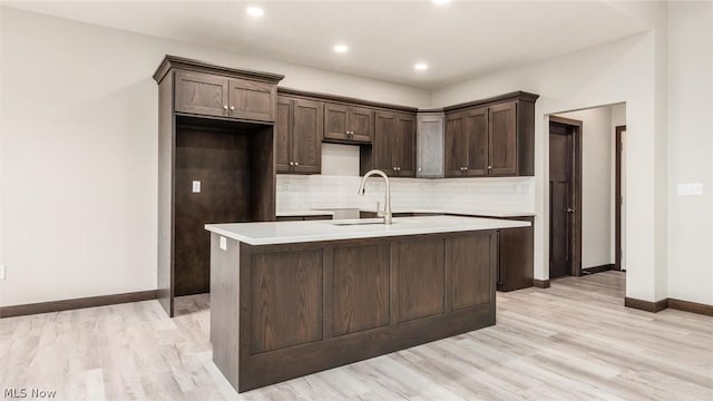 kitchen featuring sink, dark brown cabinets, light hardwood / wood-style floors, and a center island with sink