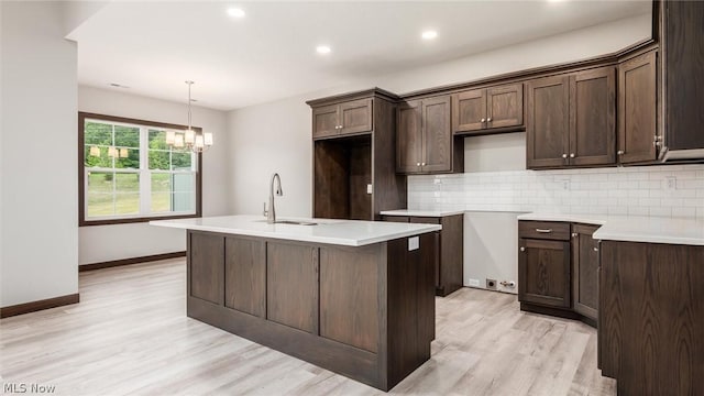 kitchen featuring sink, light hardwood / wood-style flooring, backsplash, hanging light fixtures, and a center island