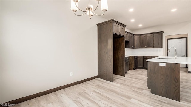 kitchen with sink, backsplash, a notable chandelier, dark brown cabinetry, and a center island with sink