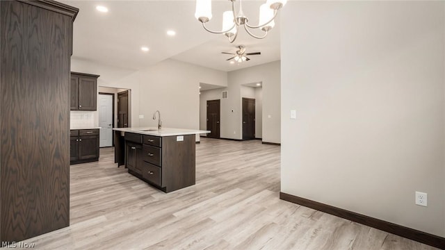 kitchen with decorative light fixtures, dark brown cabinets, light hardwood / wood-style floors, a kitchen island with sink, and ceiling fan with notable chandelier