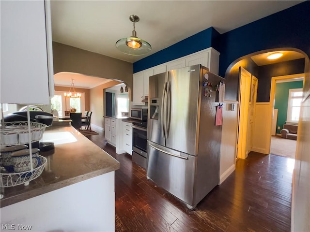 kitchen with dark wood-style floors, arched walkways, decorative light fixtures, appliances with stainless steel finishes, and white cabinets