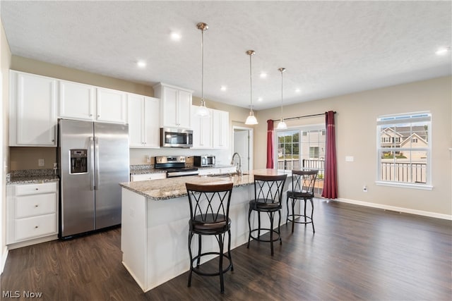 kitchen with white cabinetry, dark hardwood / wood-style flooring, an island with sink, light stone countertops, and appliances with stainless steel finishes