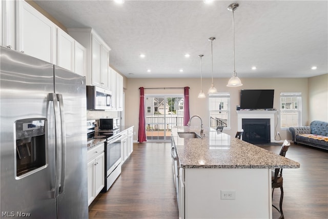 kitchen with appliances with stainless steel finishes, dark stone counters, an island with sink, white cabinetry, and dark hardwood / wood-style flooring