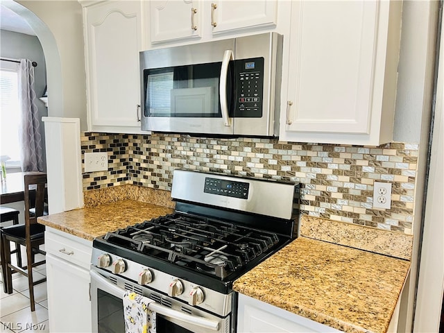 kitchen with light tile patterned floors, appliances with stainless steel finishes, white cabinetry, light stone counters, and tasteful backsplash