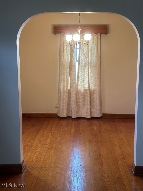 spare room featuring wood-type flooring and a notable chandelier