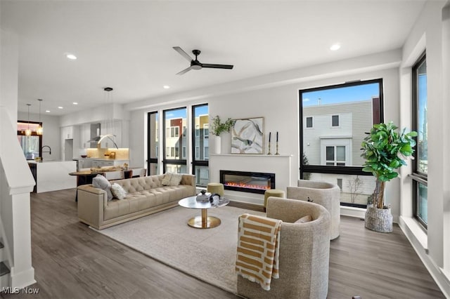 living area with a glass covered fireplace, recessed lighting, dark wood-style flooring, and ceiling fan