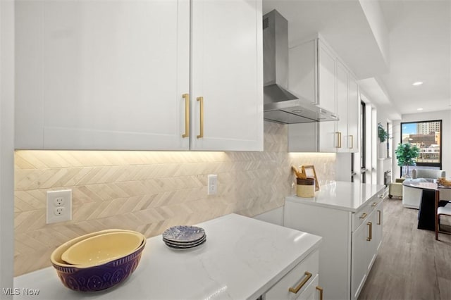 kitchen featuring wall chimney exhaust hood, white cabinets, wood finished floors, light countertops, and backsplash