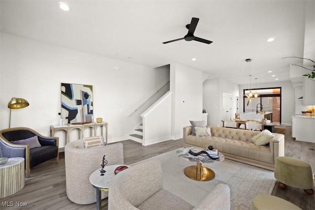 living area with baseboards, recessed lighting, stairs, light wood finished floors, and ceiling fan with notable chandelier