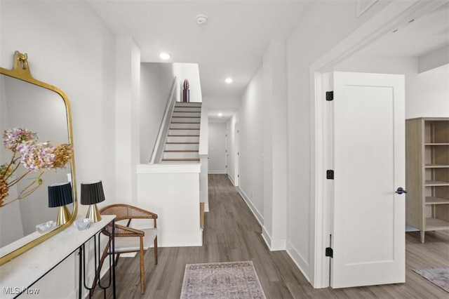 corridor featuring wood finished floors, recessed lighting, baseboards, and stairway