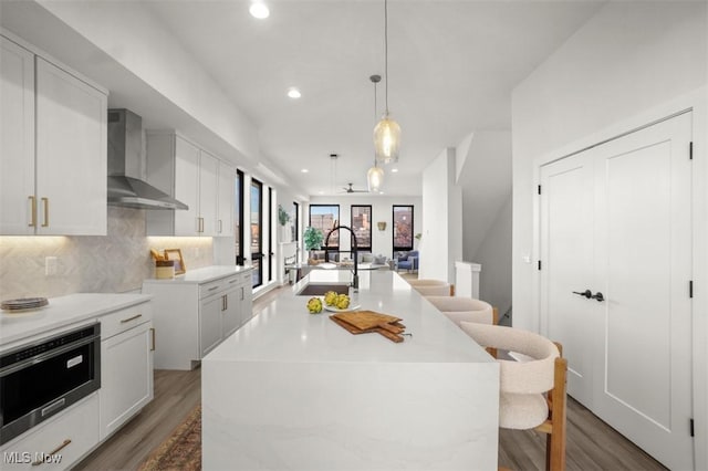 kitchen featuring a sink, wall chimney range hood, recessed lighting, light wood finished floors, and backsplash