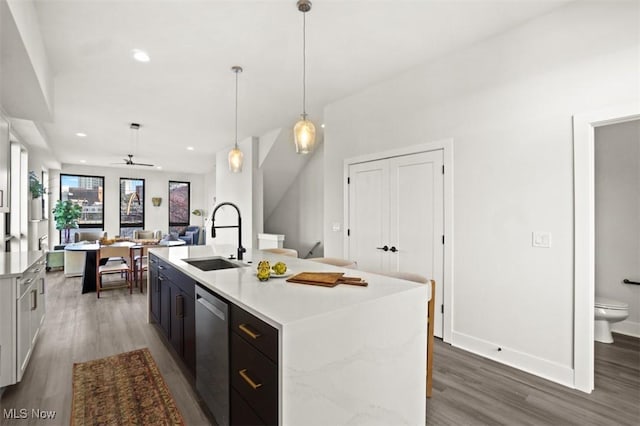 kitchen with stainless steel dishwasher, wood finished floors, a kitchen island with sink, light countertops, and a sink