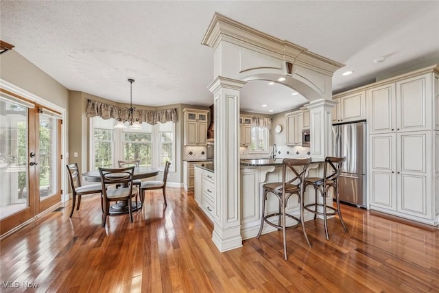 kitchen with appliances with stainless steel finishes, a kitchen bar, wood-type flooring, and decorative columns