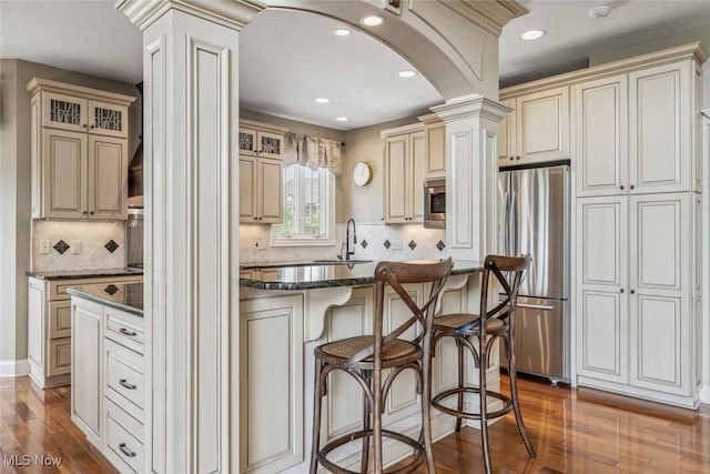 kitchen featuring cream cabinetry, a sink, wood finished floors, arched walkways, and appliances with stainless steel finishes