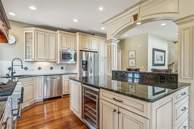 kitchen with beverage cooler, arched walkways, a sink, stainless steel appliances, and cream cabinets