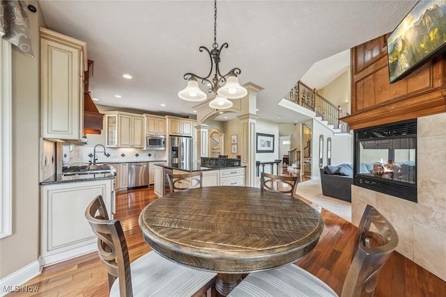 dining space featuring a multi sided fireplace, stairway, light wood-type flooring, an inviting chandelier, and ornate columns