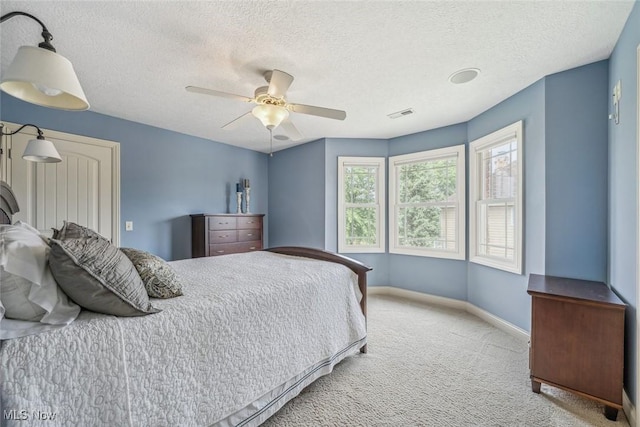 carpeted bedroom with visible vents, a textured ceiling, a ceiling fan, and baseboards