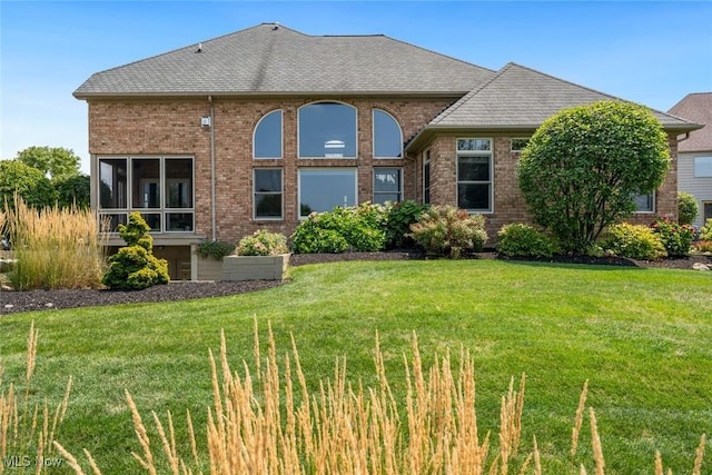 back of property featuring brick siding, a lawn, and a shingled roof