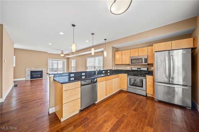 kitchen featuring pendant lighting, appliances with stainless steel finishes, a high end fireplace, and dark wood-type flooring