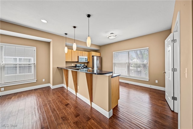 kitchen featuring decorative light fixtures, light brown cabinetry, dark hardwood / wood-style flooring, appliances with stainless steel finishes, and kitchen peninsula