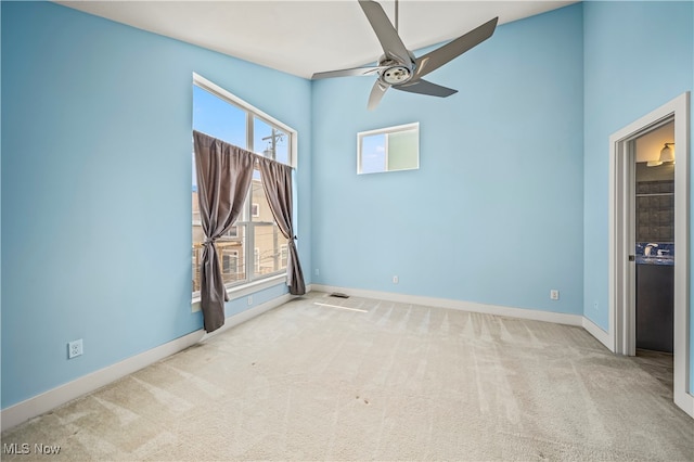 carpeted empty room with ceiling fan, a healthy amount of sunlight, and a towering ceiling