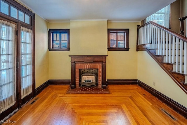 unfurnished living room with a brick fireplace, parquet floors, crown molding, and a healthy amount of sunlight