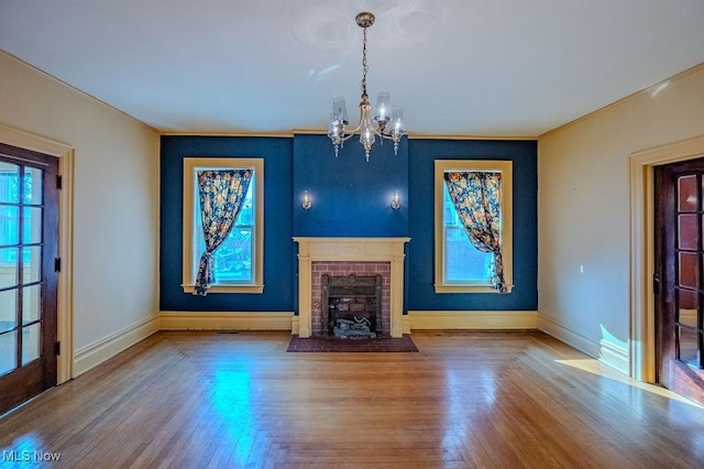 unfurnished living room featuring a brick fireplace, an inviting chandelier, and wood-type flooring